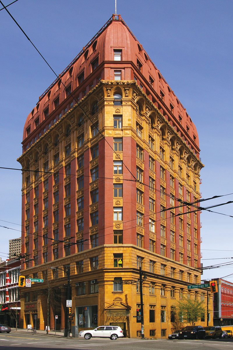 A photograph of a red and yellow bronwstone building at an intersection with a sharp angle.